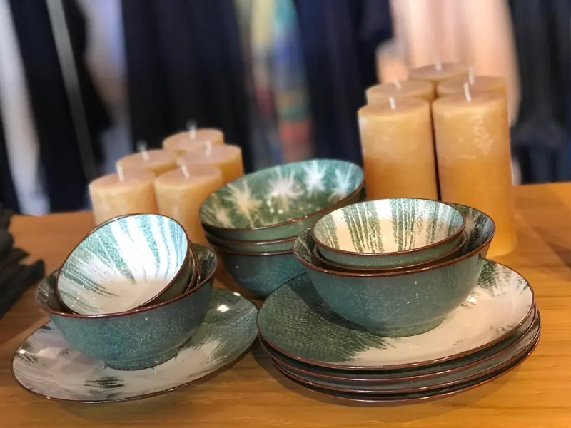 Groene schaaltjes en borden met bladmotief en okergele kaarsen op een houten tafel in de winkel