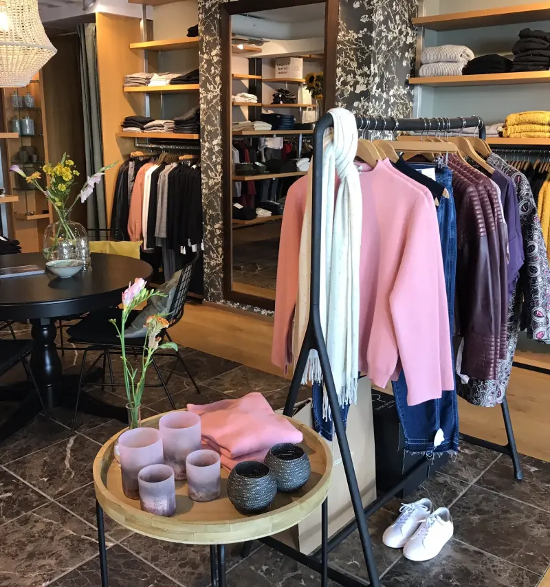 De winkel van Cogolain Bis: een kledingrek met een roze trui, eikenhouten planken vol truien en een ronde tafel met bloemen